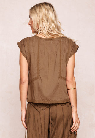 a-woman-shown-from-the-back-wearing-a-brown-short-sleeve-top-and-matching-brown-pants-against-a-light-beige-textured-background
